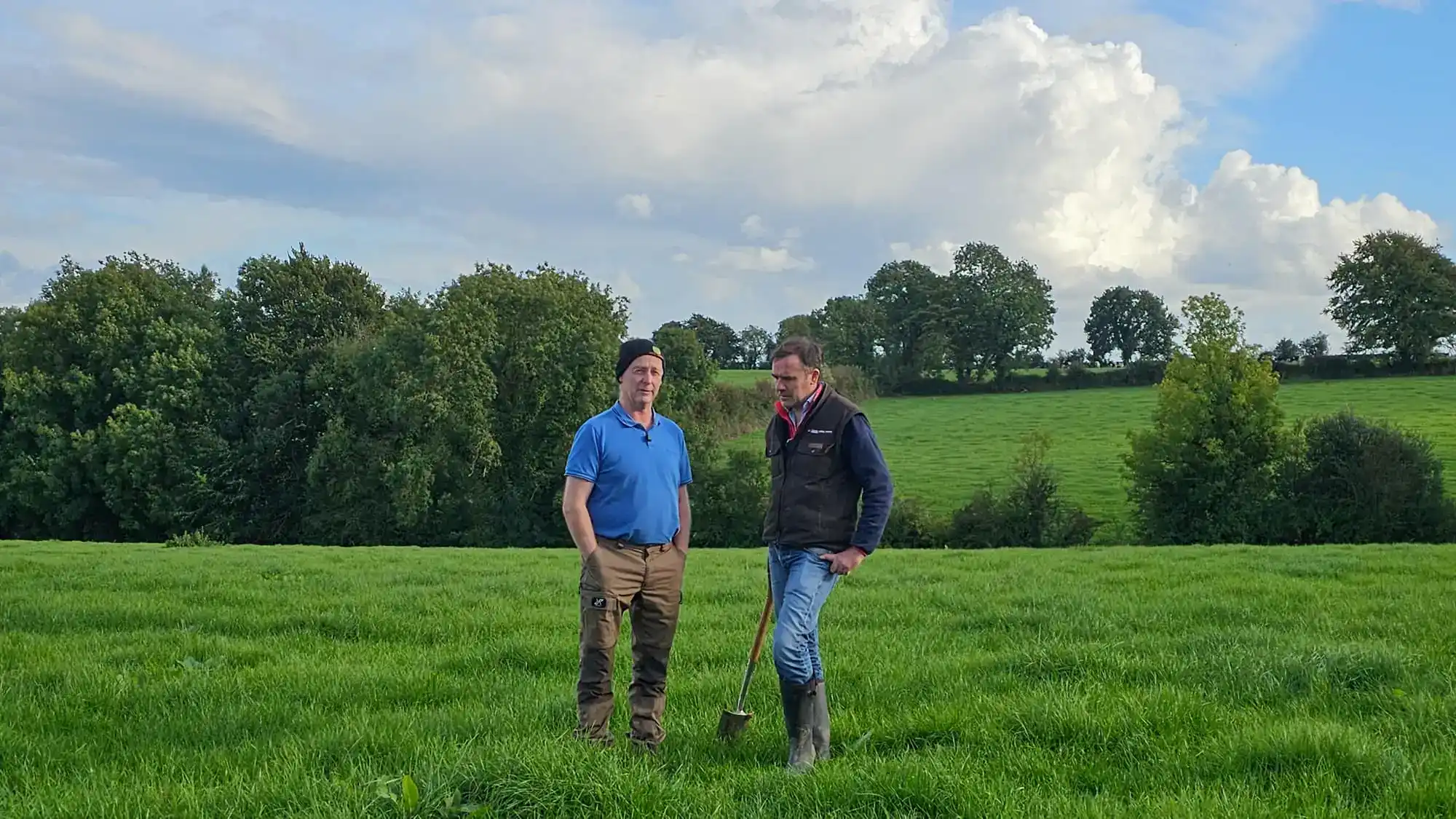 Two farmers standing in a green pasture field.