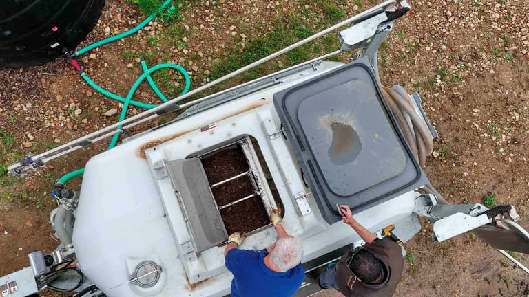 Top-down view of two operators inspecting the compost basket filled with organic material inside a Tow and Fert Multi 400 sprayer, with the tank lid open.