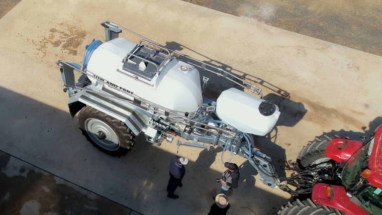 Aerial view of the Tow and Fert MultiCrop 4000 connected to a red tractor, showing its main tank, flush tank and folded spray booms.