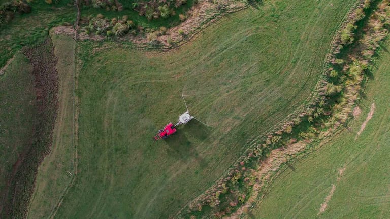 Aerial view of a red tractor towing a Tow and Fert Multi 2800 sprayer along a steep grassy hillside.