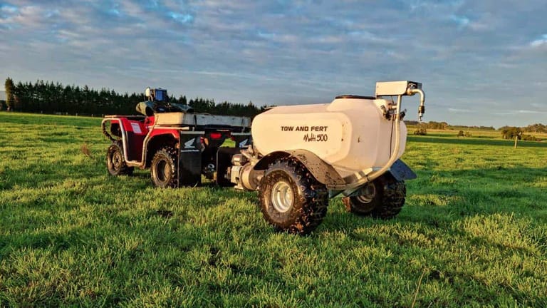 A Tow and Fert Multi 500 sprayer attached to a quad bike in a green pasture, with the sprayer's tank, pump and wheels clearly visible.