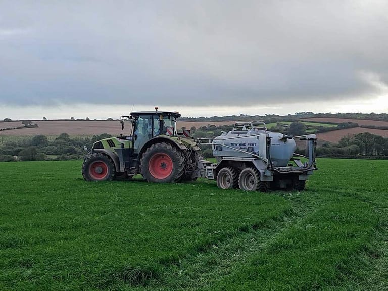 A tractor towing a Tow and Fert Multi 4000 fertiliser sprayer across a green pasture, with rolling farmland in the background.
