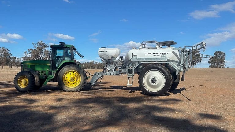 Tow and Fert MultiCrop 4000 sprayer connected to a John Deere tractor, with its spray booms unfolded in a dry field.