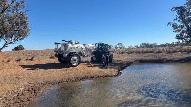 Tow and Fert MultiCrop 4000 sprayer connected to a tractor, drawing water from a farm pond through a suction hose.