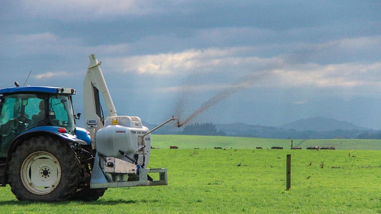 A Tow and Fert Multi 1200 sprayer applying liquid fertiliser across a green pasture through a spray boom.