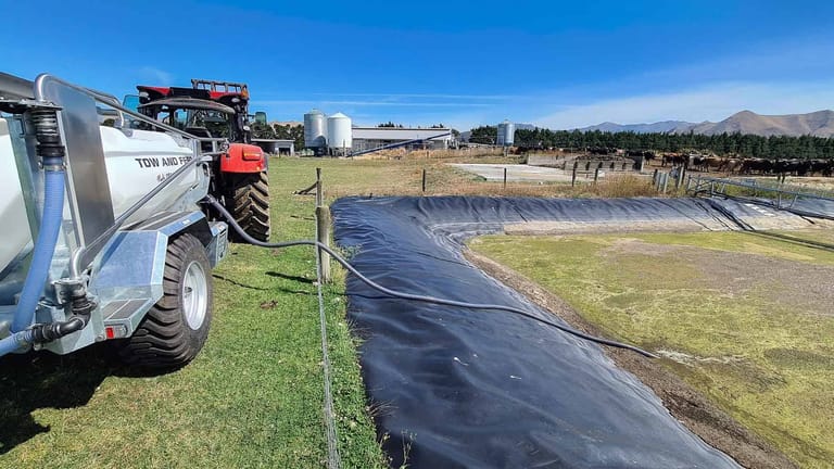 Tow and Fert Multi 2800 connected to a red tractor, drawing water from a lined farm pond through a suction hose.